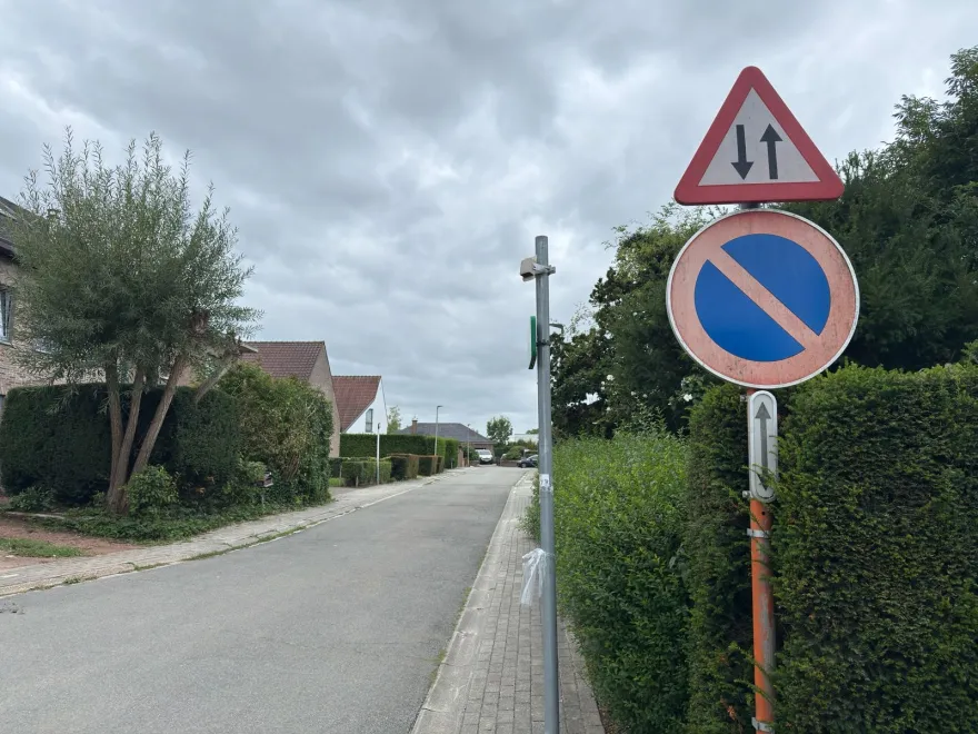 Triangle de danger à deux flèches opposées, au-dessus d'un signal de stationnement interdit, dans une rue résidentielle