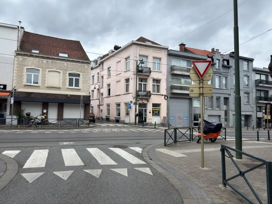 Signal cédez-le-passage et triangles blancs au sol devant un carrefour bruxellois traversé de rails de tram