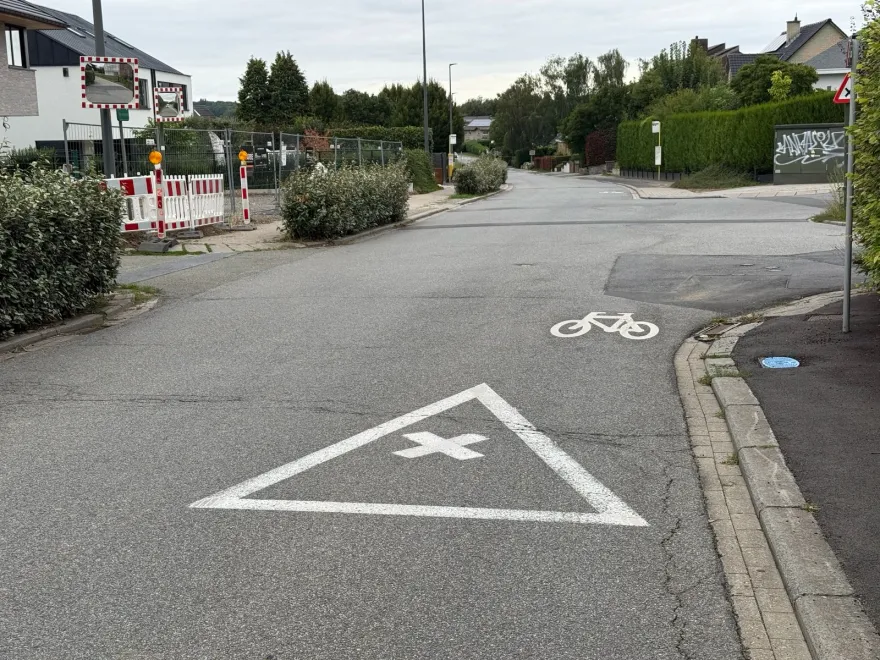 Vélo peint directement sur l'asphalte d'une rue, sans ligne de séparation, à l'approche d'un carrefour