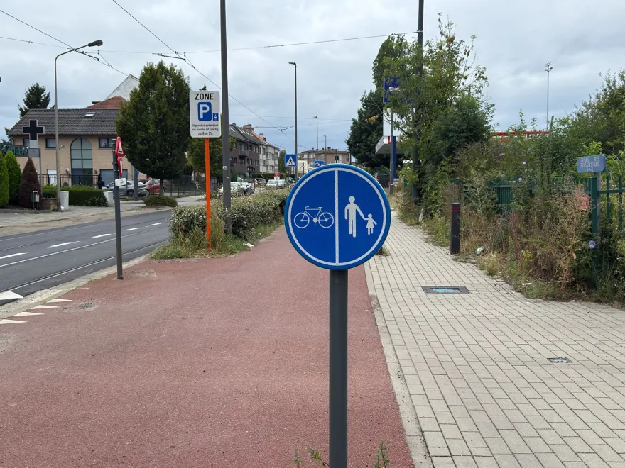 Signal rond bleu divisé en deux, un vélo à gauche et des piétons à droite, au bord d'une piste cyclable rouge