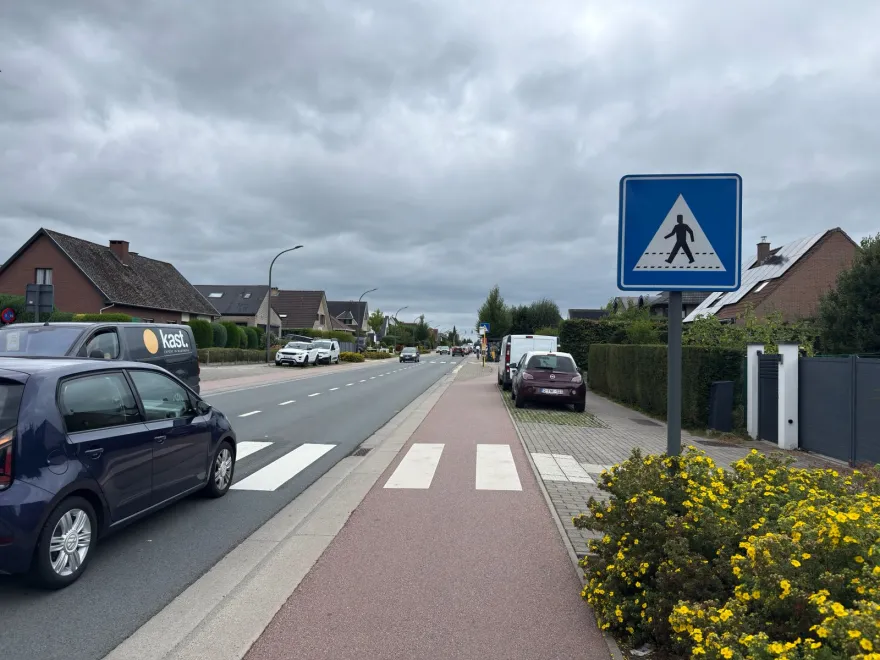 Piste cyclable rouge longeant une chaussée, avec un passage pour piétons et son signal carré bleu